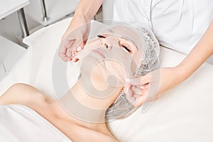 Beautician smoothes sheet mask on woman face for rehydrate face skin, procedure in beauty salon