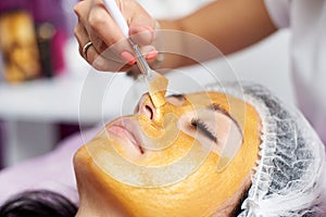 Beautician with special brush puts on face girl golden mask