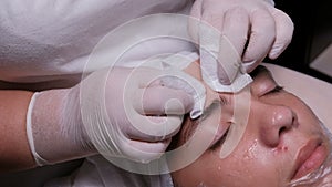 Beautician squeezes acne on the forehead of a teenage boy. Closeup of hands in white gloves in beauty clinic. Male client gets fac