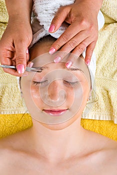 Beautician tweezing woman eyebrows