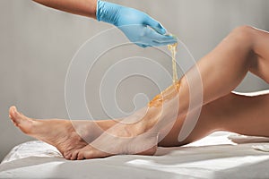 Beautician waxing female legs with liquid sugar paste in spa center.