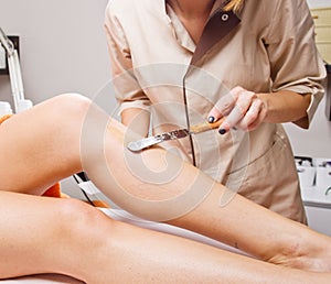Beautician waxing a woman`s leg