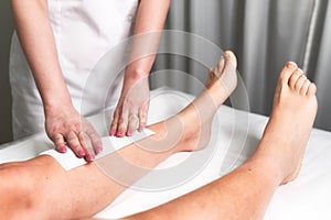 Beautician waxing a woman`s leg applying a strip of material over the hot wax to remove the hairs