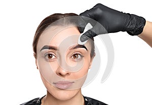 Beautician wiping tint from woman`s eyebrows on white background, closeup