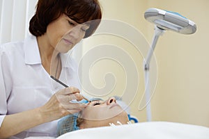 Beautician works with eyebrow of woman.