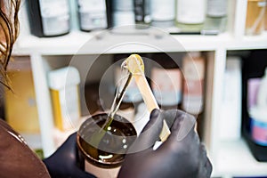 Beauticians hand with glove holding wooden spatula with depilation wax