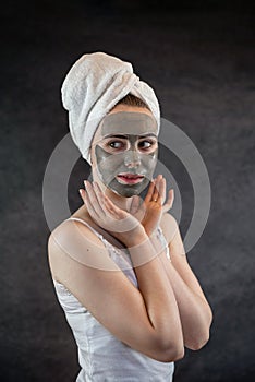 Beautifu woman wear white towel with green clay facial mask look at camera isolated on black