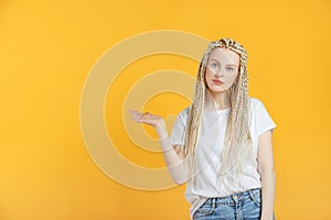 Beautiful 30 year old woman with braids kanekalon hairstyle point to copy space on yellow background