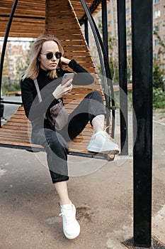 Beautiful 30-year-old woman with glasses is texting and taking selfies on a smartphone camera in a park, outdoors