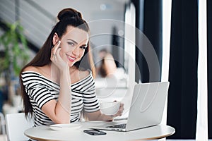 Beautiful adult female is sitting and holding her laptop while looking at the camera.