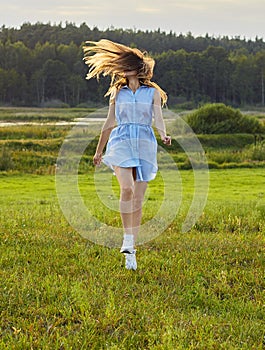 Beautiful adult girl jumping in the wild nature: meadow, lake and forest