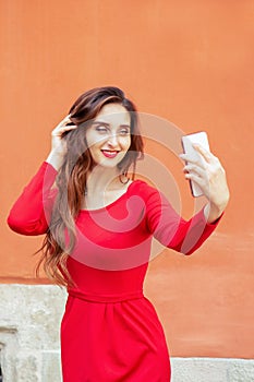 Beautiful adult girl is making selfie by smartphone on orange background