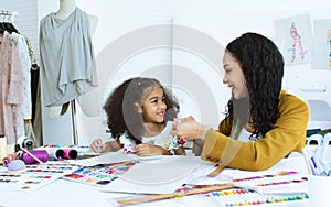 Beautiful adult mother teaching, bonding her mixed race African little cute daughter girl using sewing machine for making dress,
