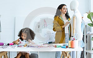 Beautiful adult mother teaching, bonding her mixed race African little cute daughter girl using sewing machine for making dress,