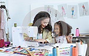 Beautiful adult mother teaching, bonding her mixed race African little cute daughter girl using sewing machine for making dress,