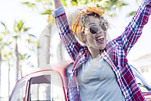 Beautiful adult woman exult excited outdoor with red car and palms trees in background - summer style vacation travel lifestyle photo