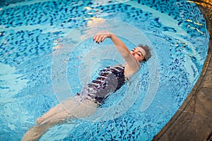 Beautiful adult woman in striped swimsuit swimming in blue pool on her back at resort. Sport activity health concept.