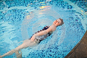 Beautiful adult woman in striped swimsuit swimming in blue pool on her back at resort. Sport activity health concept.