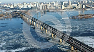 Beautiful aerial shot, car traffic moving across frozen winter Dnepr river over long bridge in sunrise Kyiv, Ukraine.