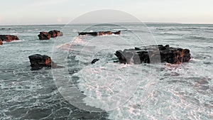 A beautiful aerial view of black rocks at ocean shore at golden hour. Ocean reef coast line panoramic footage at sunset