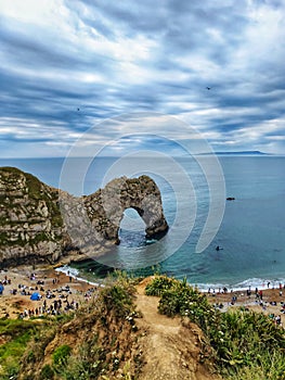 Beautiful aerial view of the Durdle Door arch surrounded by the bay water under gloomy clouds