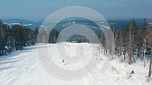 Beautiful aerial view of people on a ski slope starting to skiing down of a track near coniferous trees and cable car