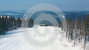 Beautiful aerial view of people on a ski slope starting to skiing down of a track near coniferous trees and cable car