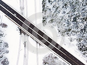 Beautiful aerial view of snow covered fields with a two-lane road among trees. Scenic winter landscape near Vilnius, Lithuania