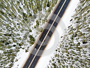 Beautiful aerial view of snow covered fields with a two-lane road among trees. Scenic winter landscape near Vilnius, Lithuania