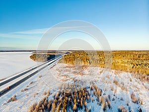 Beautiful aerial view of snow covered fields with a two-lane road among trees. Scenic winter landscape near Vilnius, Lithuania