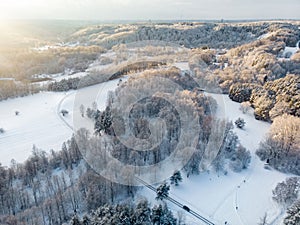 Beautiful aerial view of snow covered pine forests and a road winding among trees. Rime ice and hoar frost covering trees. Winter