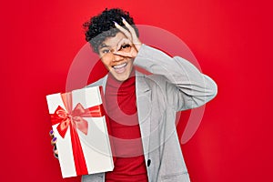 Beautiful african american afro business woman holding gift over isolated red background with happy face smiling doing ok sign