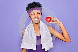 Beautiful african american afro sporty woman doing exercise wearing towel holding heart with a happy face standing and smiling