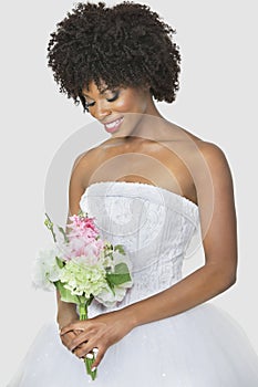 Beautiful African American bride holding bouquet over gray background