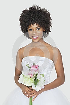 Beautiful African American bride holding bouquet over gray background