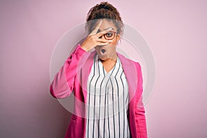 Beautiful african american businesswoman wearing jacket and glasses over pink background peeking in shock covering face and eyes