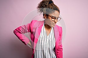 Beautiful african american businesswoman wearing jacket and glasses over pink background Suffering of backache, touching back with