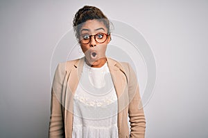 Beautiful african american businesswoman wearing jacket and glasses over white background afraid and shocked with surprise