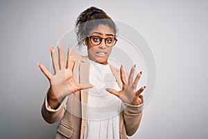 Beautiful african american businesswoman wearing jacket and glasses over white background afraid and terrified with fear