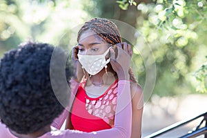 Beautiful African-American girl helps her friend to put a face mask on. Face covering is important to protect from