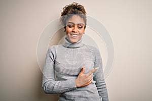 Beautiful african american girl wearing turtleneck sweater standing over white background cheerful with a smile of face pointing