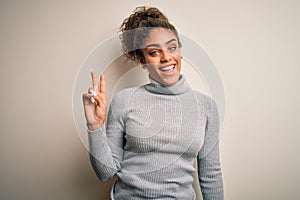 Beautiful african american girl wearing turtleneck sweater standing over white background showing and pointing up with fingers