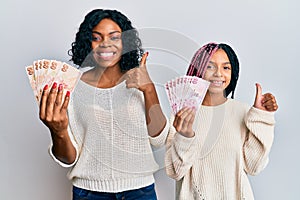 Beautiful african american mother and daughter holding turkish lira banknotes smiling happy and positive, thumb up doing excellent