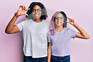 Beautiful african american mother and daughter wearing casual clothes and glasses smiling and confident gesturing with hand doing