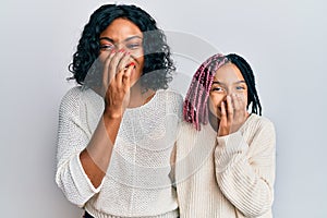 Beautiful african american mother and daughter wearing casual clothes and hugging laughing and embarrassed giggle covering mouth