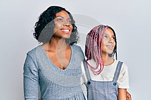 Beautiful african american mother and daughter wearing casual clothes and hugging looking away to side with smile on face, natural
