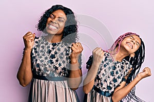 Beautiful african american mother and daughter wearing sexy party dress very happy and excited doing winner gesture with arms