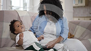 Beautiful African American mother playing video games with hyperactive toddler son. Positive young woman and cute boy