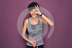 Beautiful african american sporty woman doing exercise controlling weight using tape measure with happy face smiling doing ok sign