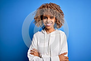 Beautiful african american sporty woman wearing casual sweatshirt over blue background happy face smiling with crossed arms